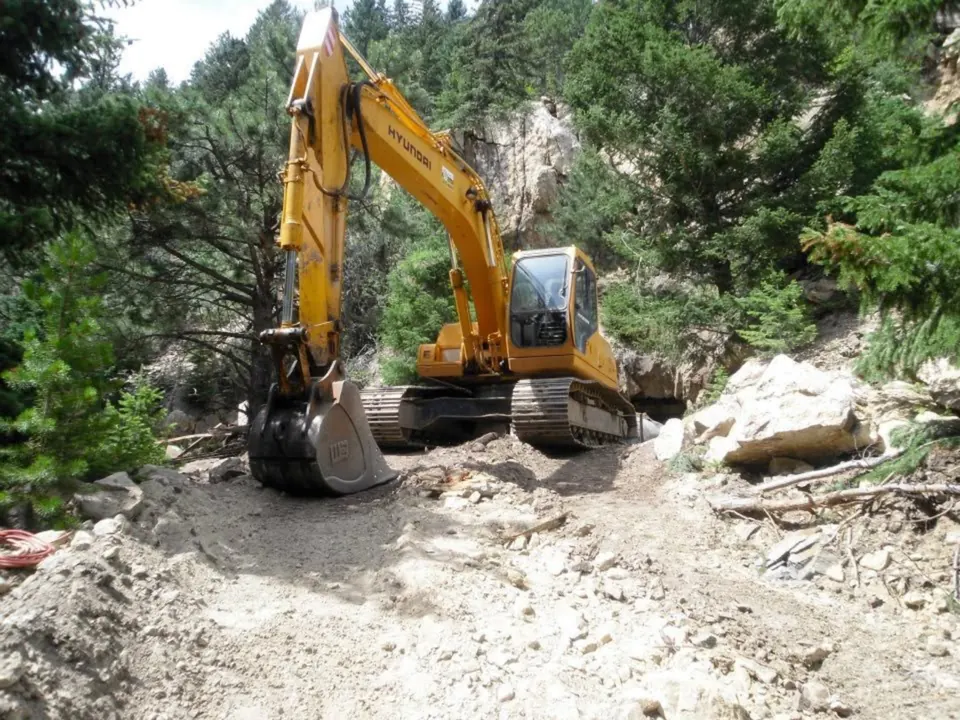 Hyundai excavator working a rocky cut in a pine canyon