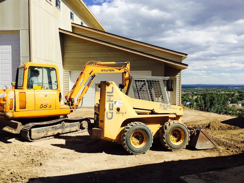 Mini excavator and Gehl skid steer working beside a new house, downtown Denver on the horizon