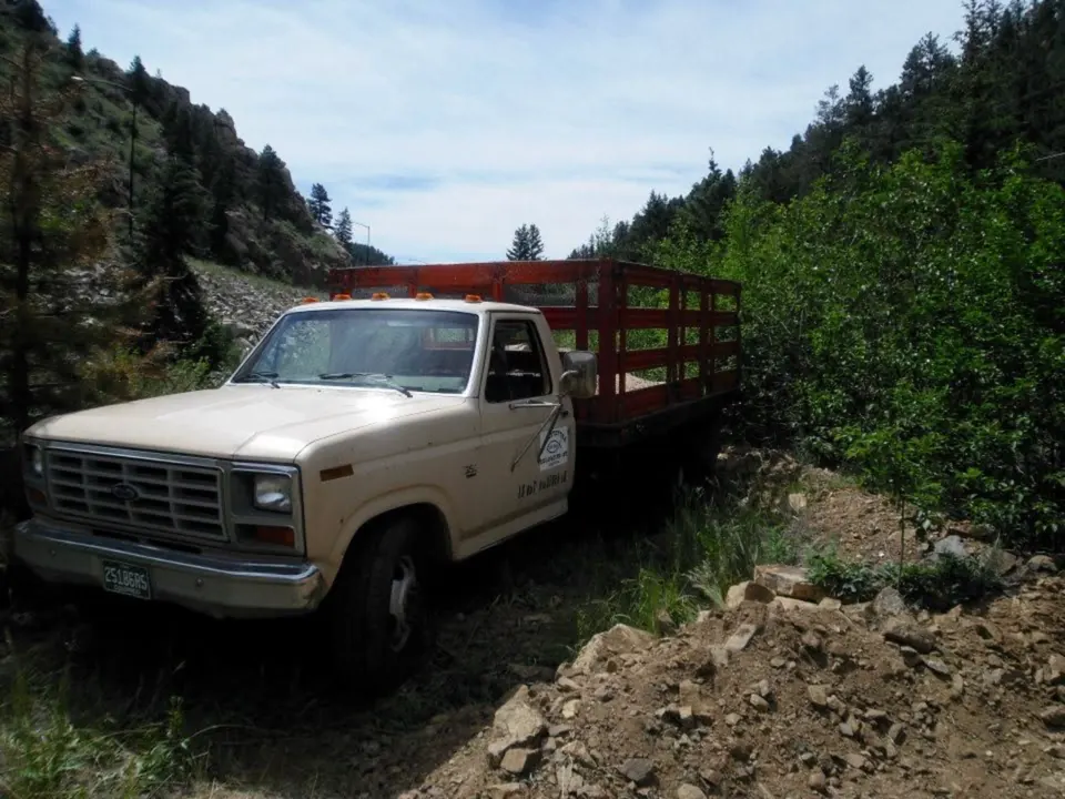 Cream Ford stake-bed truck with red rails on a canyon road, Ramstetter logo on the door